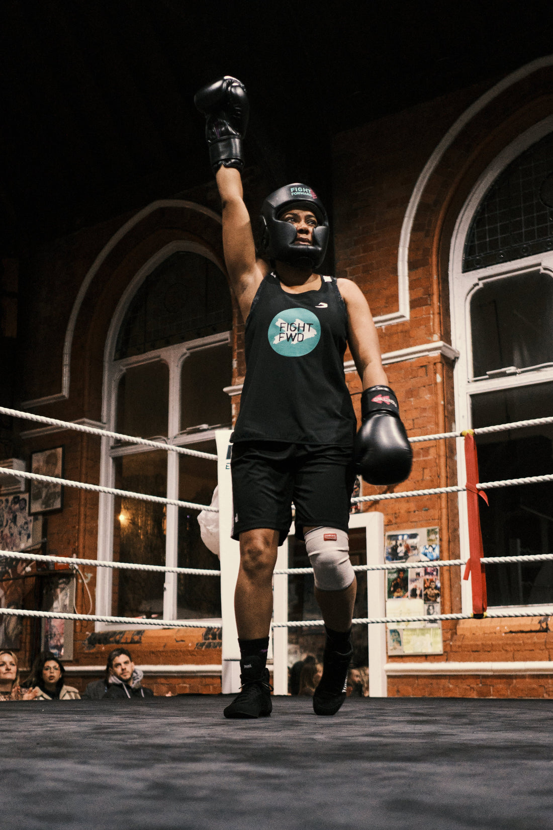 A Black woman stands in a boxing ring with her glove raised high, embodying strength and resilience. 