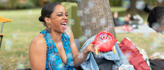 Image of black woman and artist Amja sitting in a park with a bubble machine in her hands
